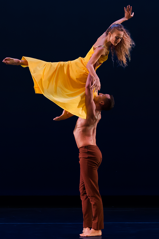 the woman in yellow floats above her partner as he holds her waist with his extended arms. She appears to be laughing. Her hair swings with her