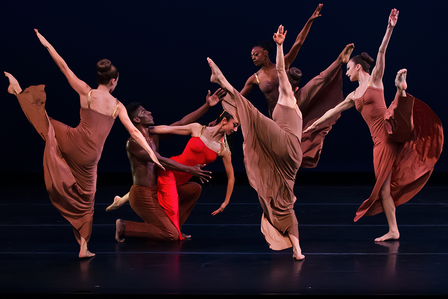 a chorus of high kicking women surround red love who is supported by her male partner on his knees