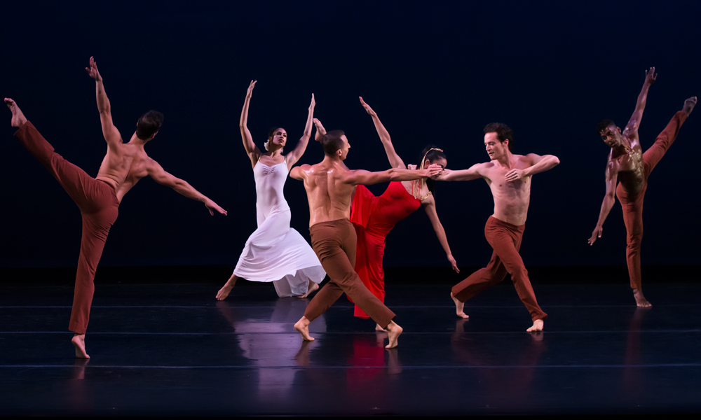 the woman in white and the woman in red dance in the background as the chorus converses with eachother through movement 