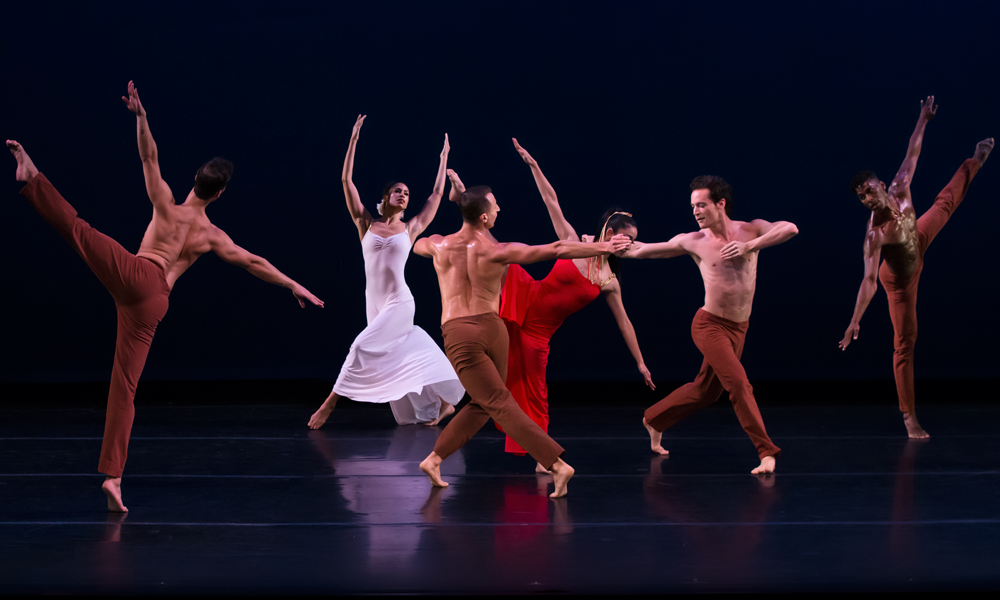 the woman in white and the woman in red dance in the background as the chorus converses with eachother through movement