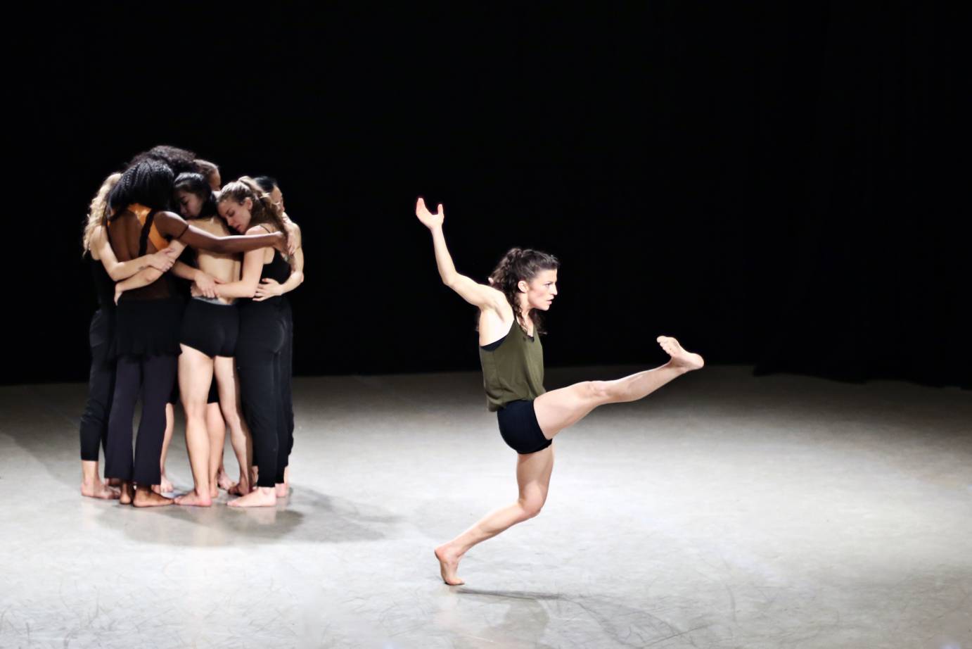 One solo dancer kicks while a group of women hug in the background