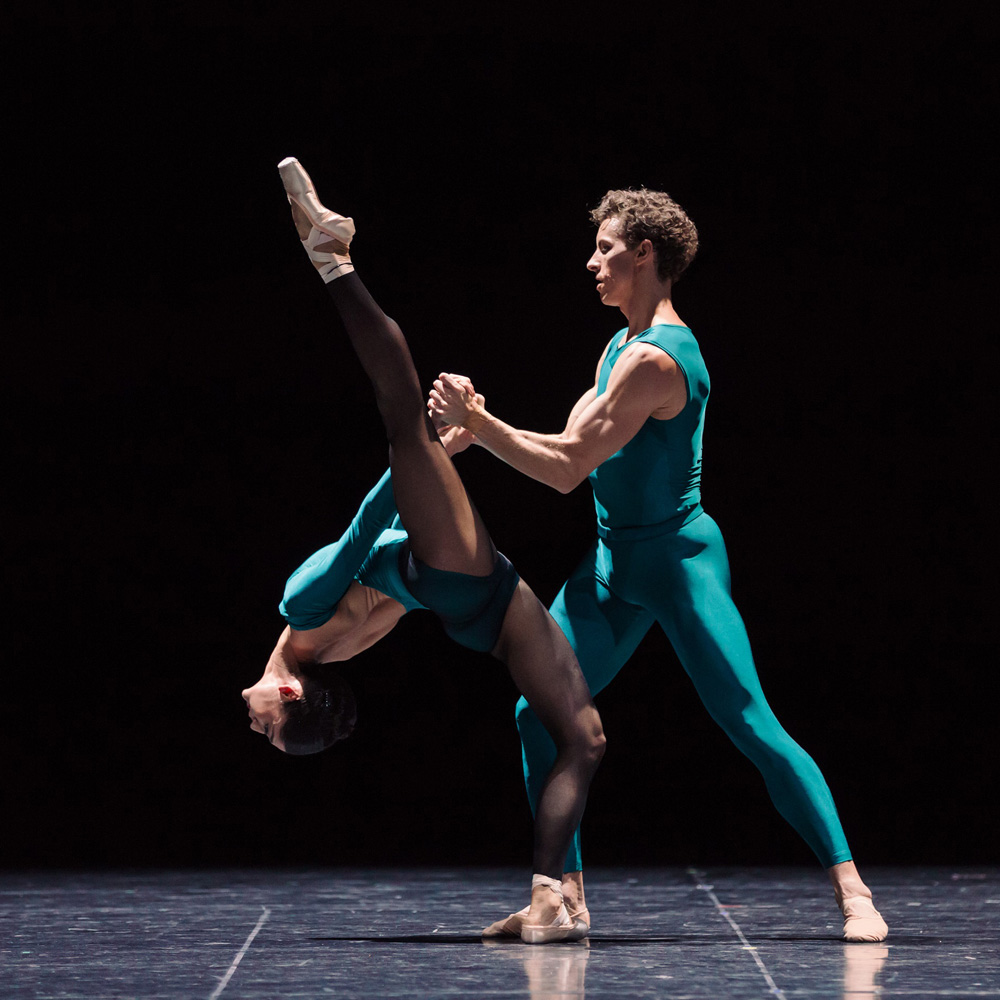 A man and woman clasp their hands to hold on as she dramatically dips back. Her head nearly touching the floor while one leg extends to the ceiling.