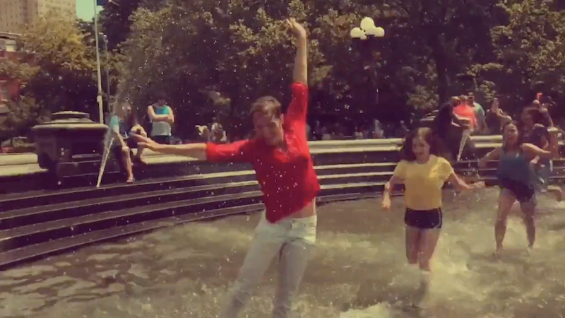 A woman in red playfully splashes in a fountain.