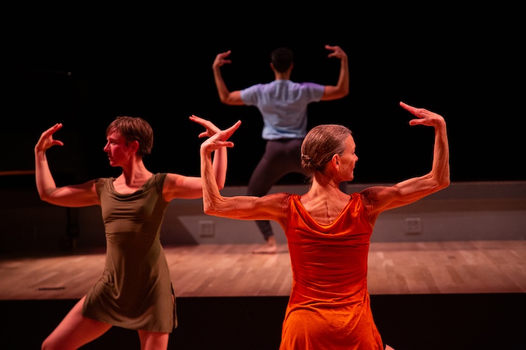 a trio on different levels of the stage one facing us the other 2 showing  us their backs. They extend their arms outward to their  sides outward as if supporting an imaginary basking on the shoulders .