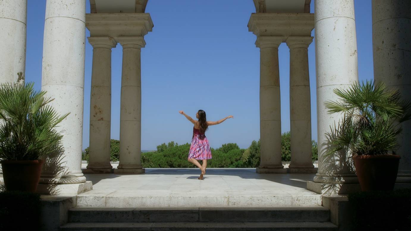 Catherine Coury, back turned, dancing in between columsn