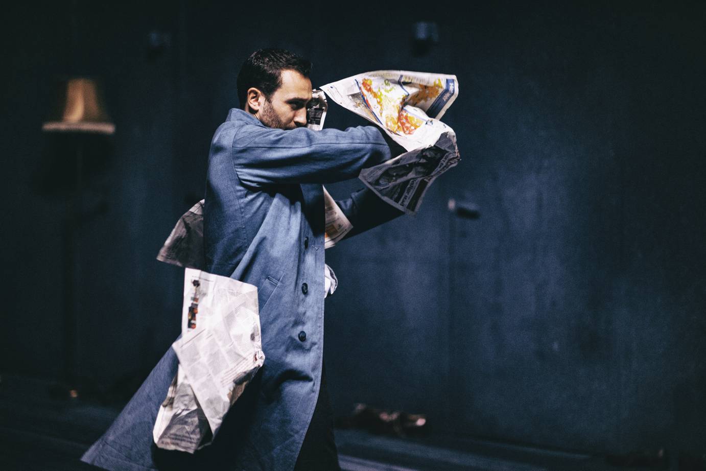 A newspaper wraps itself around a man in a denim jumpsuit