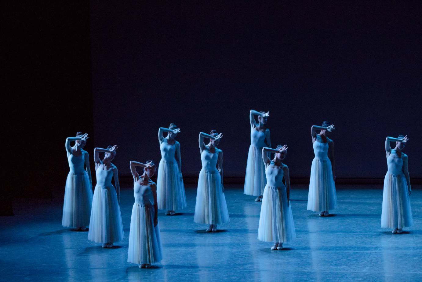 A group of blue clad women press their wrist to their forehead