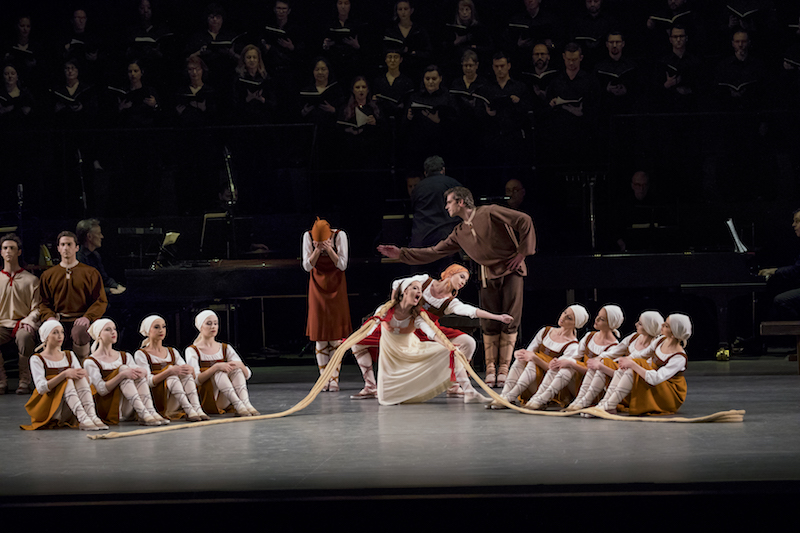 A woman wears a long braided wig sitting in the middle of a line of dancers. 