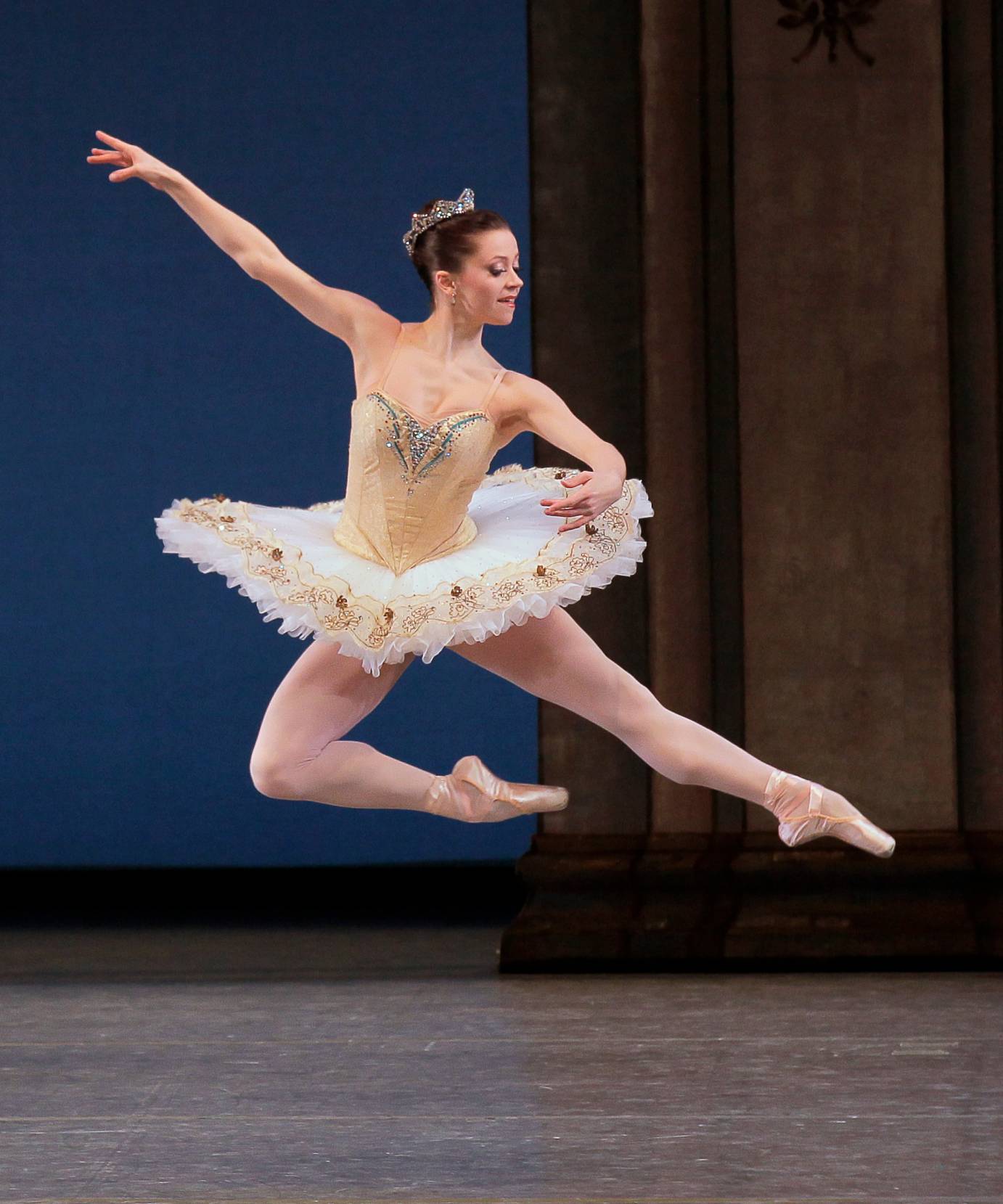 A woman in a gold tutu leaps sideways in profile