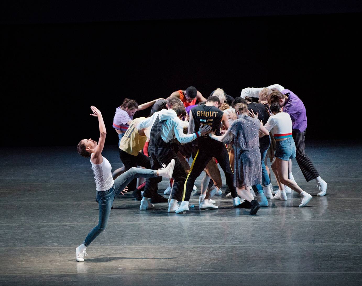 A woman downstage affects as jazzy posture against a clump in the background