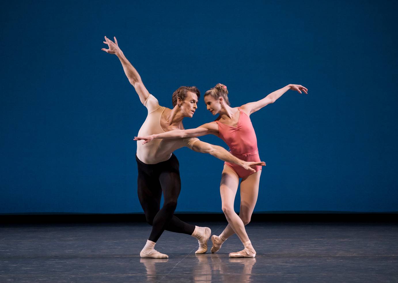 A man and a woman cross arms, the others extended, as they bend their knees in a jazzy plie