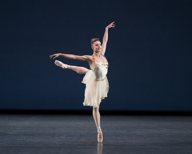 Sara Mearns in a white chiffon dress stands en pointe in attitude position