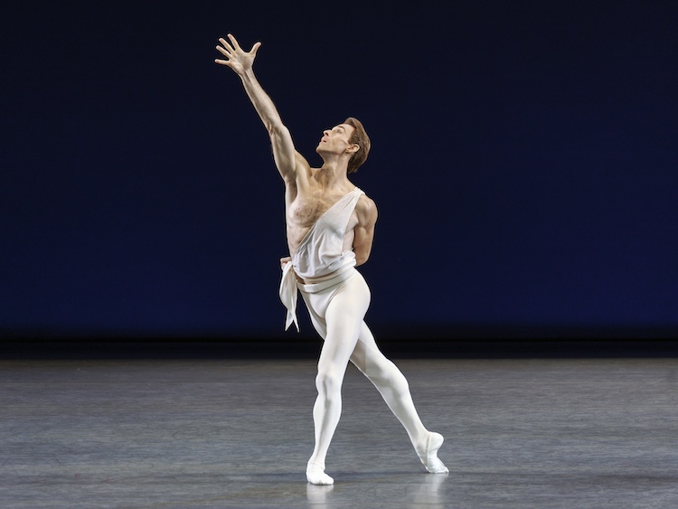 man in white tights and sash like white top reaching to the sky