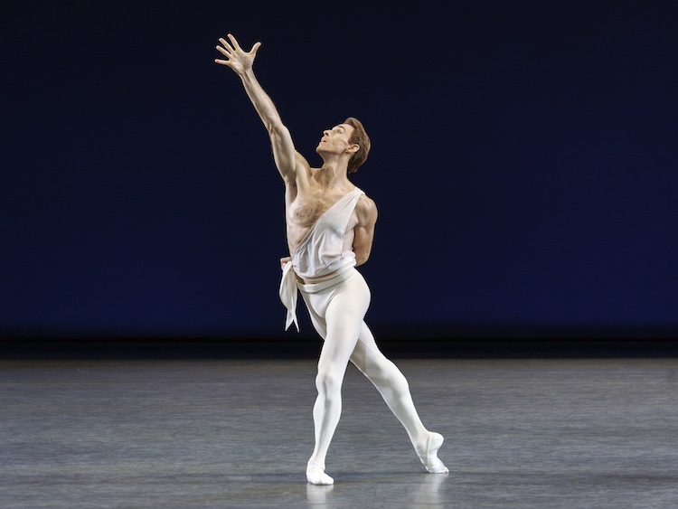 man in white tights and sash like white top reaching to the sky 