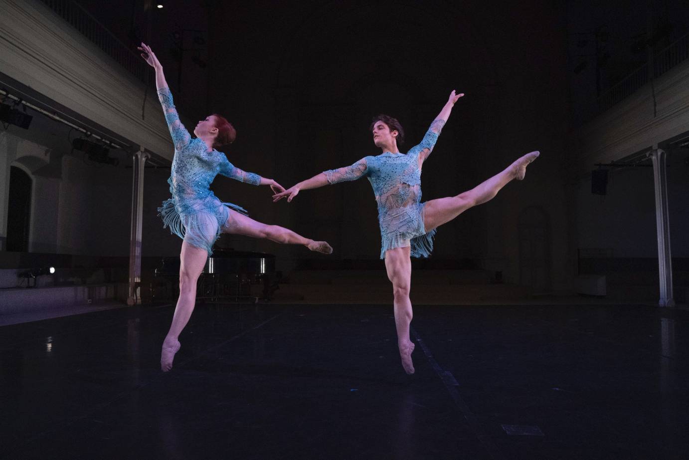 A man and a woman jump with a leg extended, feet pointed