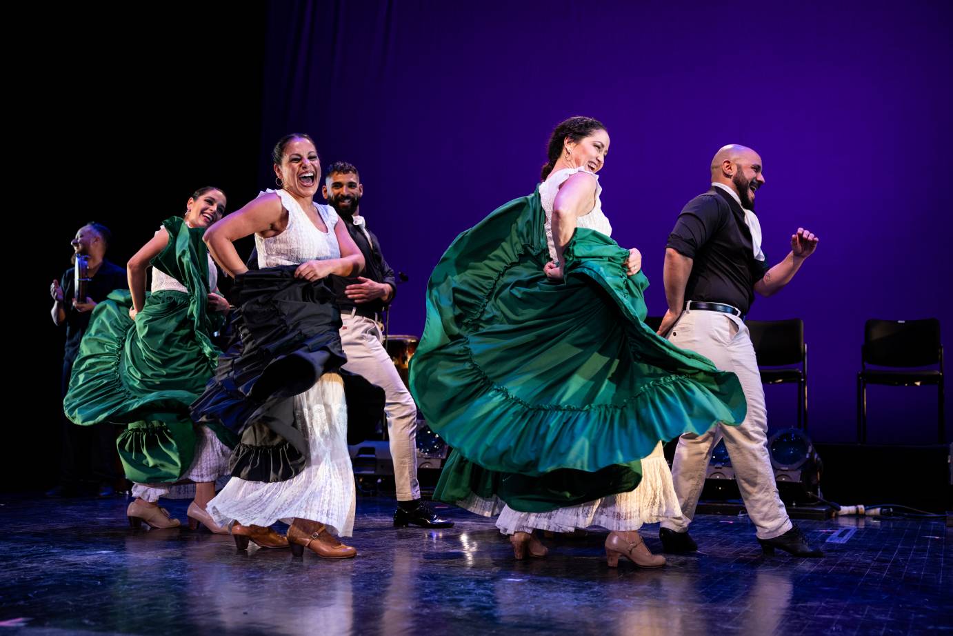 company of jubilant dancers, men and women, entering the stage laughing and dancers