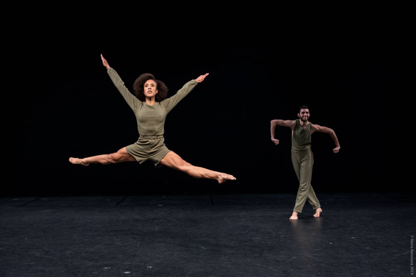 One woman scissors her limbs in a leap while a man hunches over