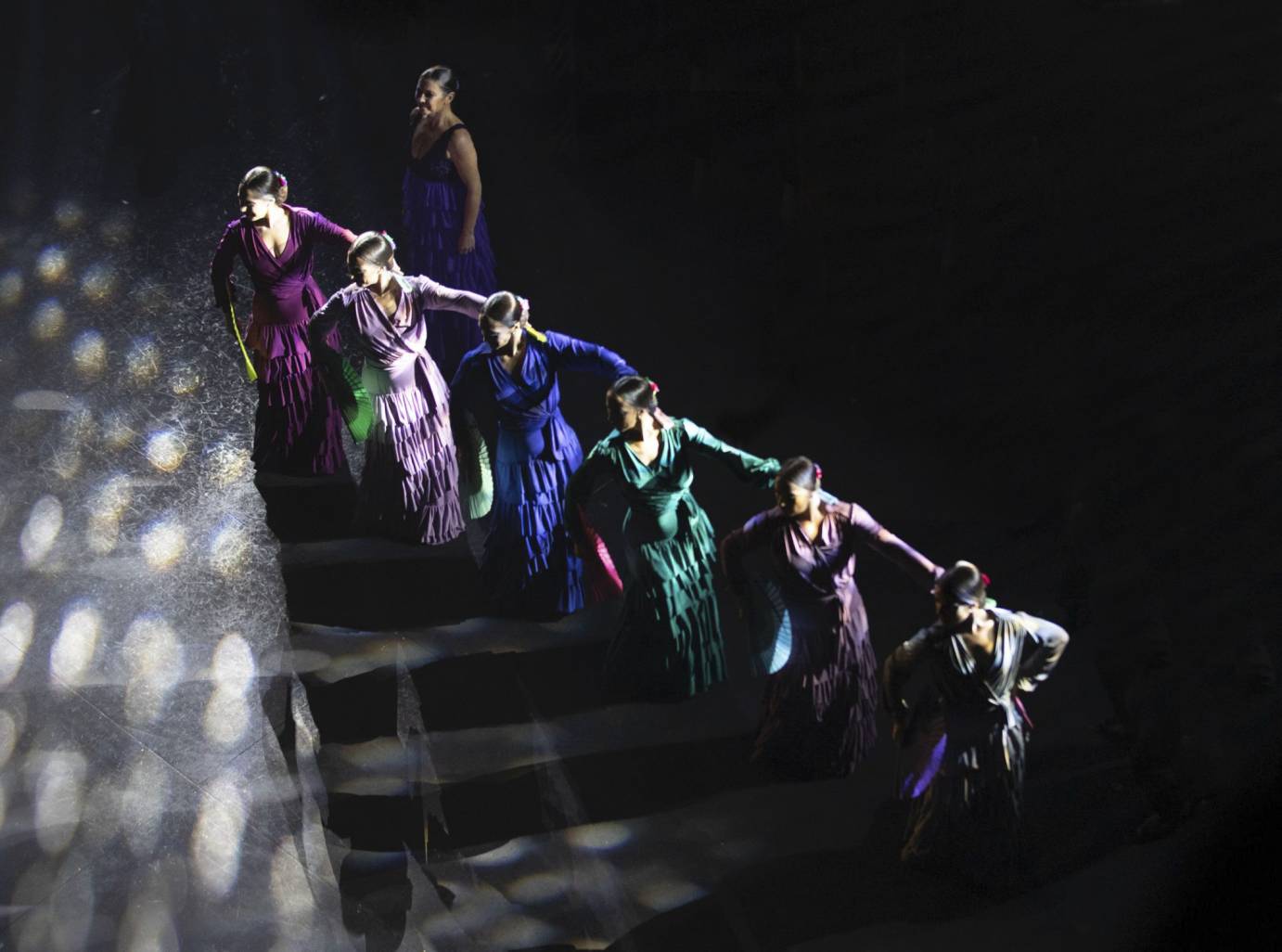 A line of women dancers in purple, blue, and green dresses, seen from above.
