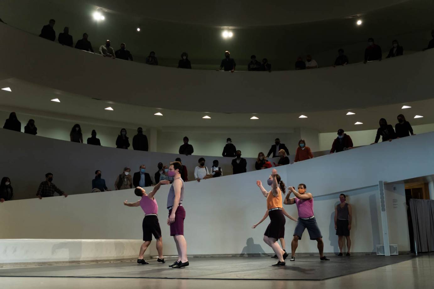 Two dancers lift their arms rapturously as two stand in profile; people watch from above