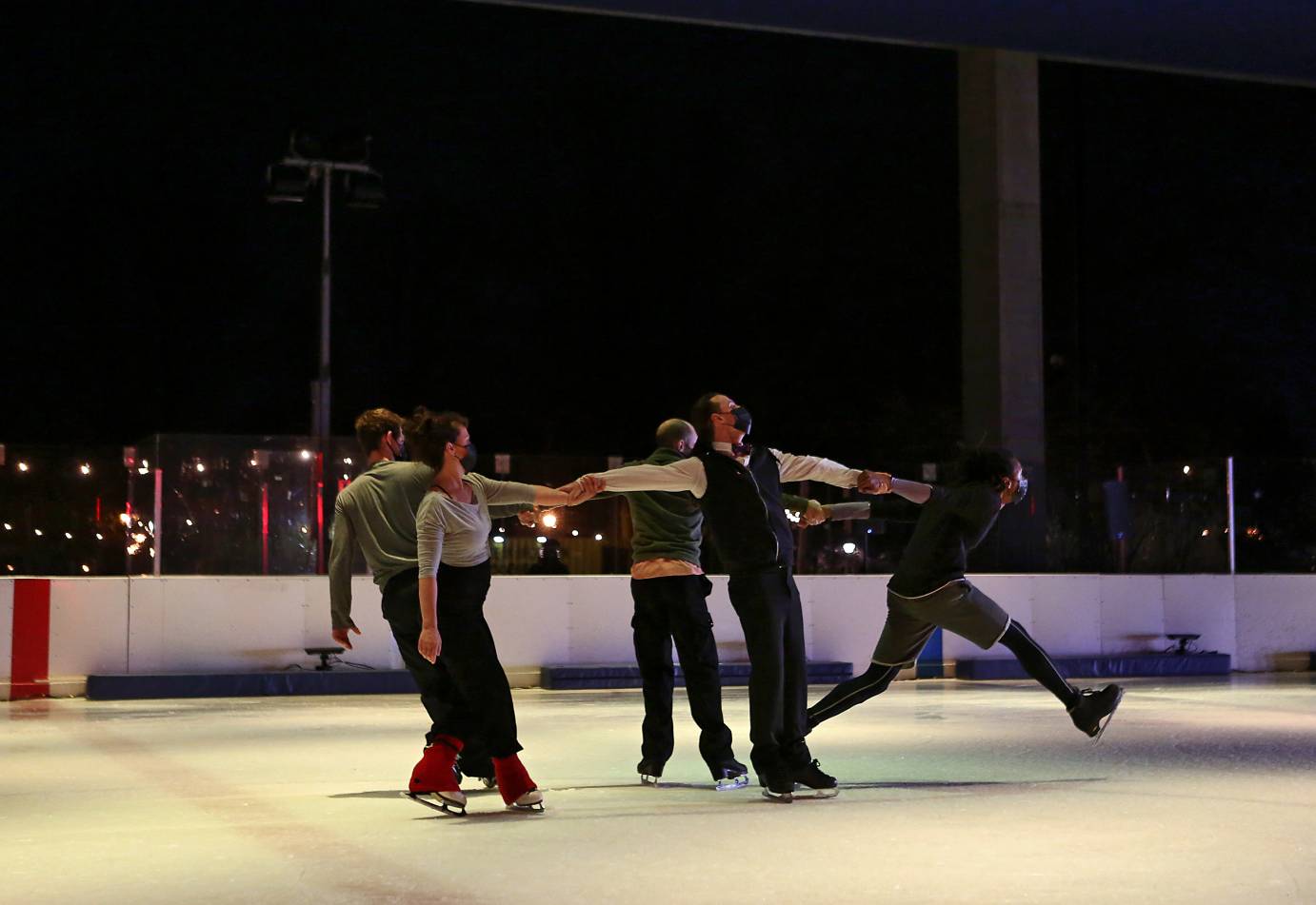 Five skaters hold hands to create a loose circle as one tries to break free