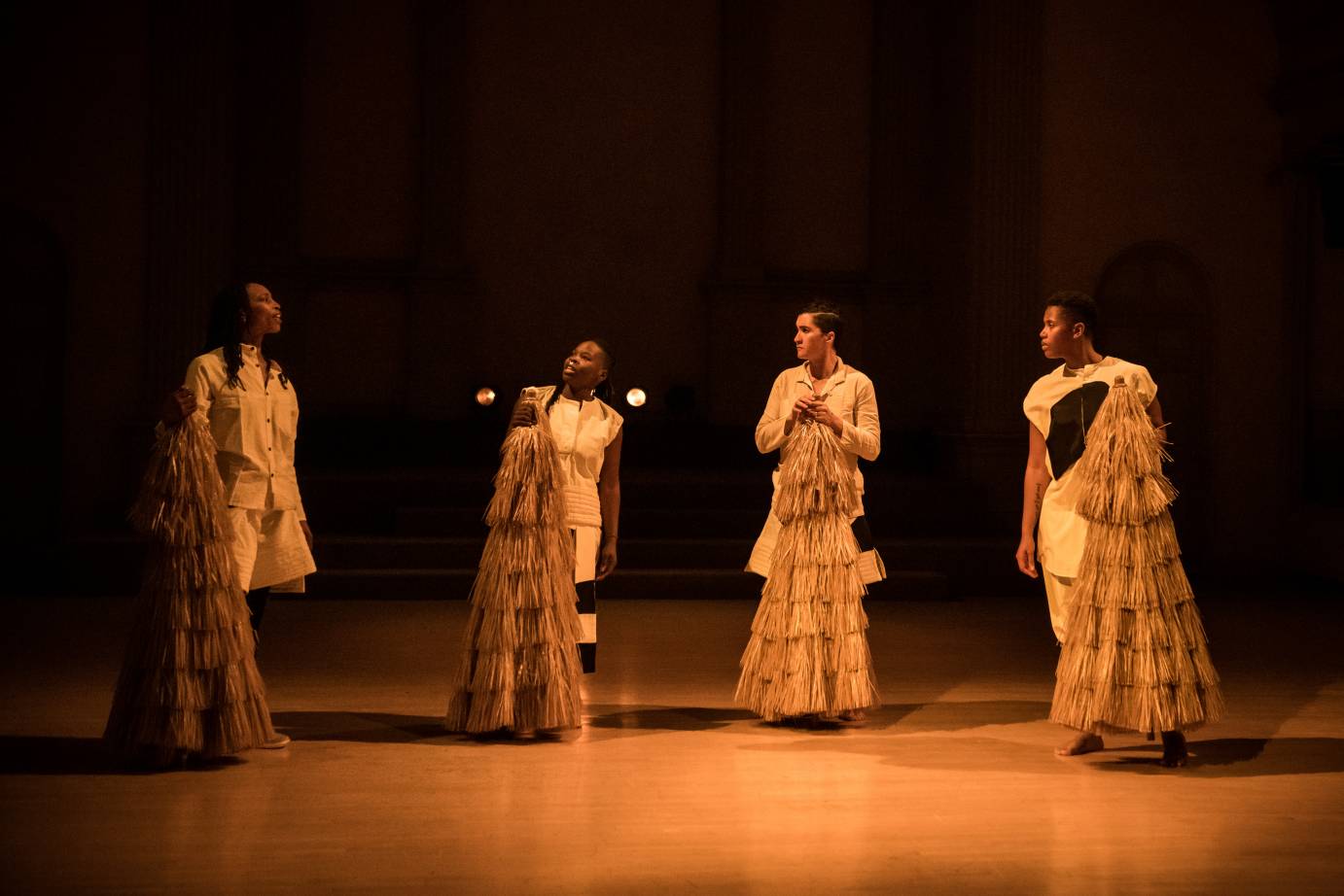 Four dancers hold raffia cones in their hands