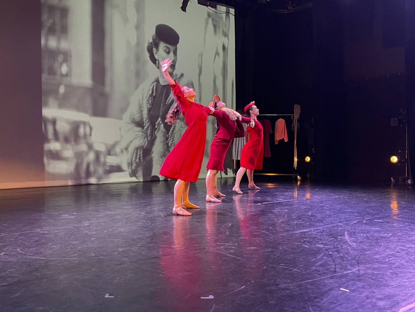 dancers in red dresses and matching pillbox hats  in front of a Gordon Parks black and white fashion photo