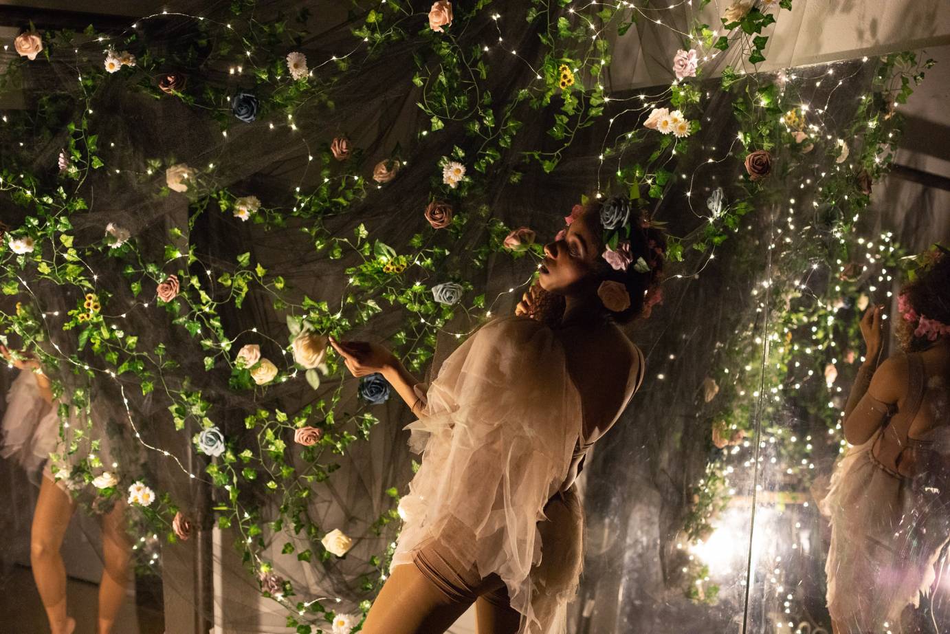 A woman poses among silk roses and twinkle lights