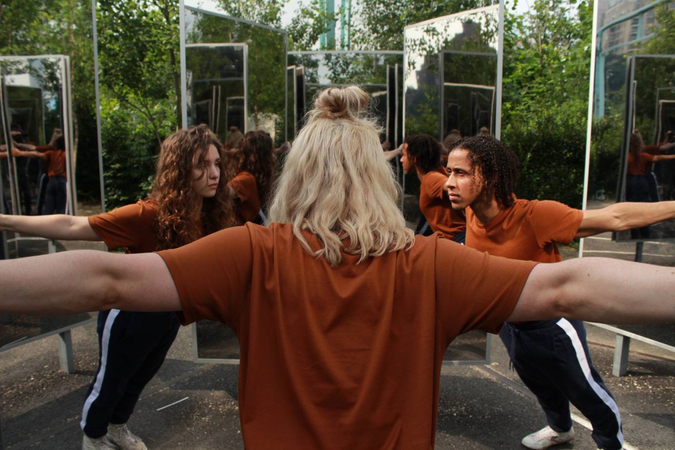 Dancers in burnt orange shirts lean forward, their arms extended