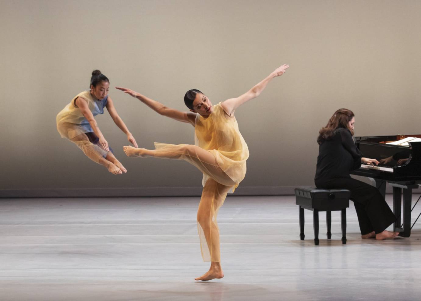 One dancer executes a pike jump while another is in a torqued attitude