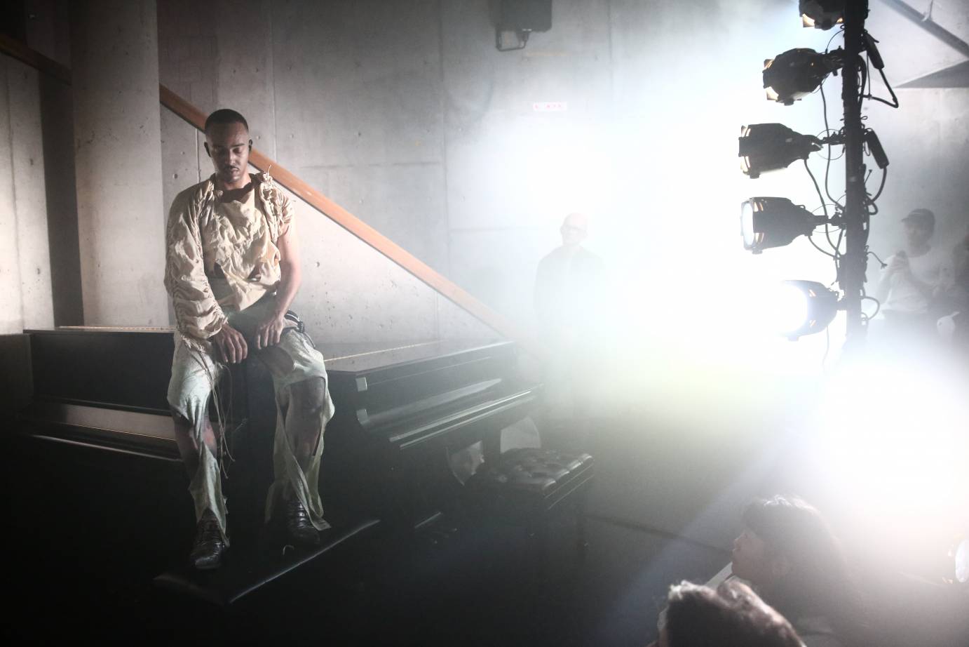 Paul Maheke sits in a piano, bathed in light