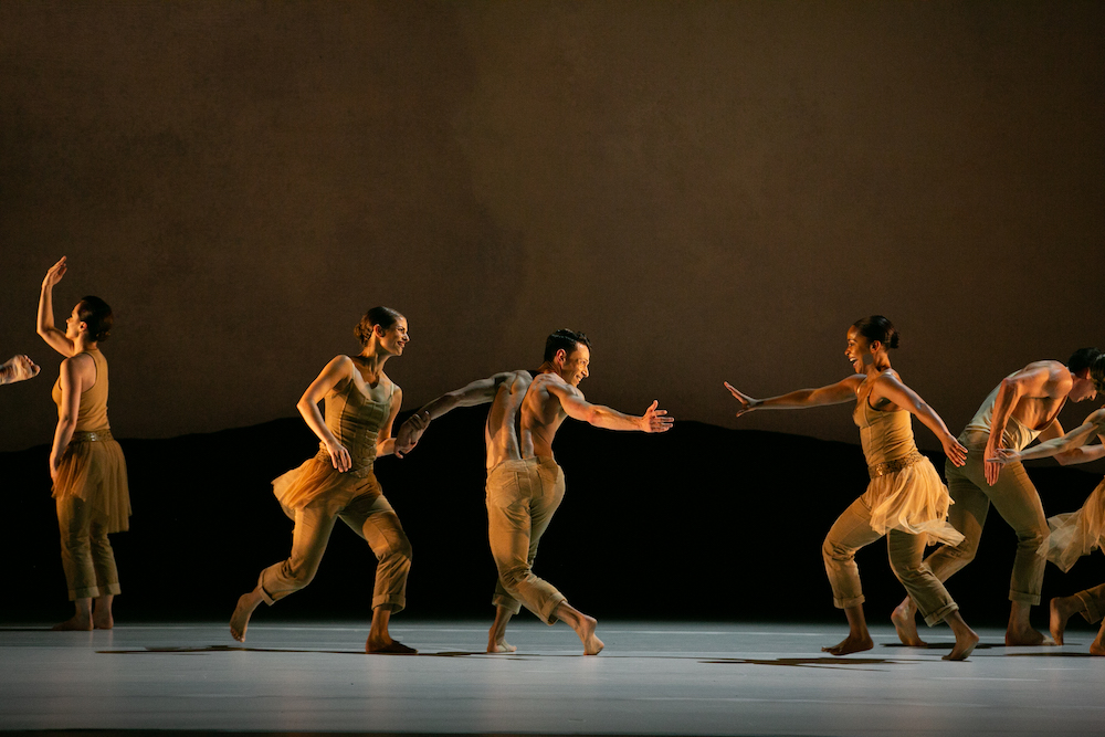 the company runs and greets each other on a golden lit stage wearing gold colors 