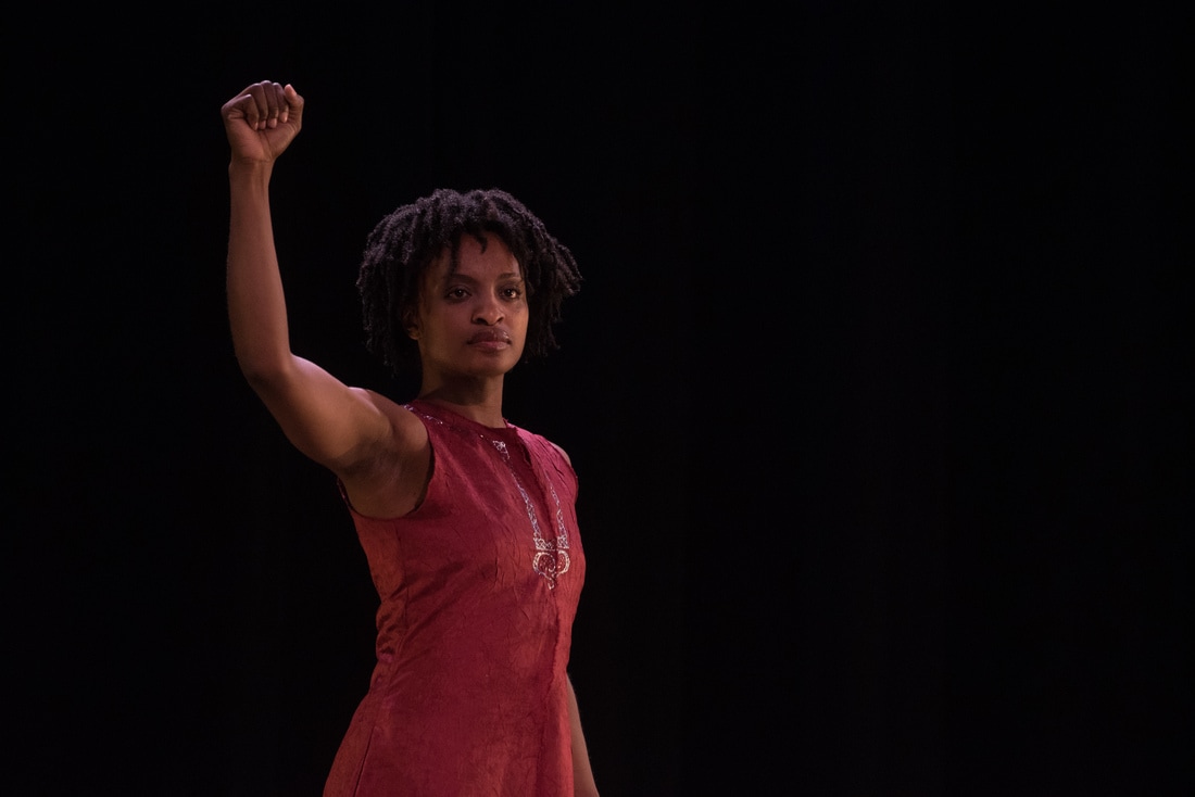 Davalois Fearon a blak woman in red shor dress with her right hand extended upward abover her in a fist