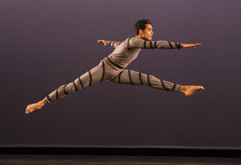 A dancer leaps into the air as if he's jumping over a fence.