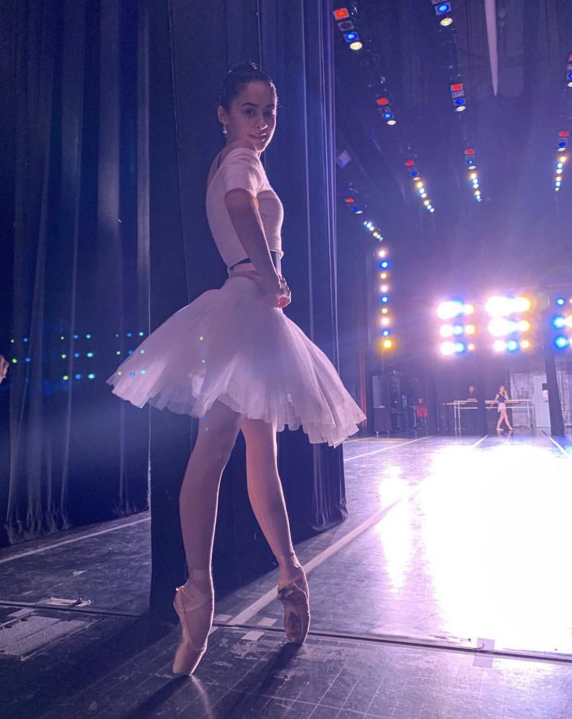 A dancer in a white tutu waits in the wings