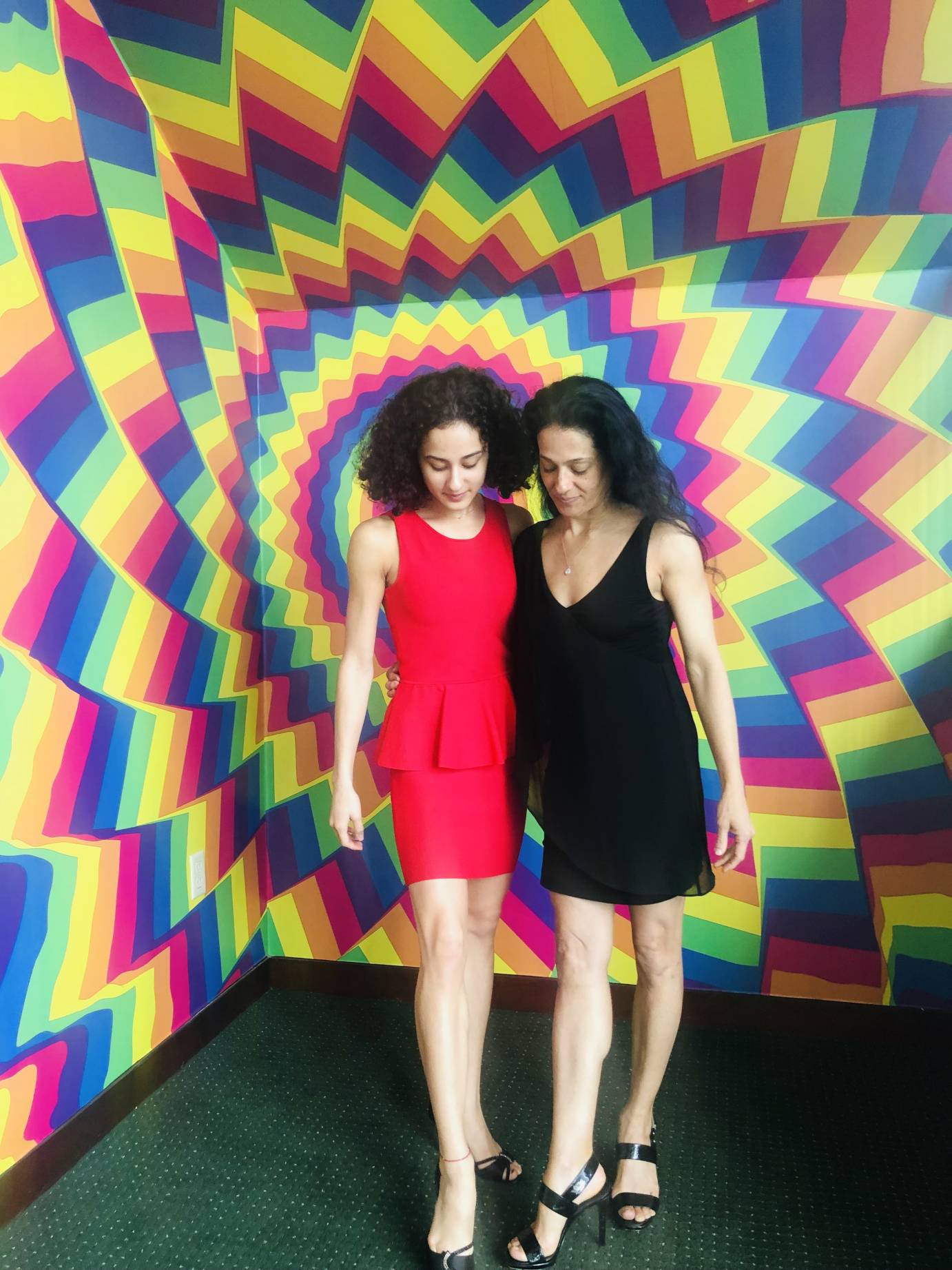 A mom and a daughter stands against a spiky rainbow background