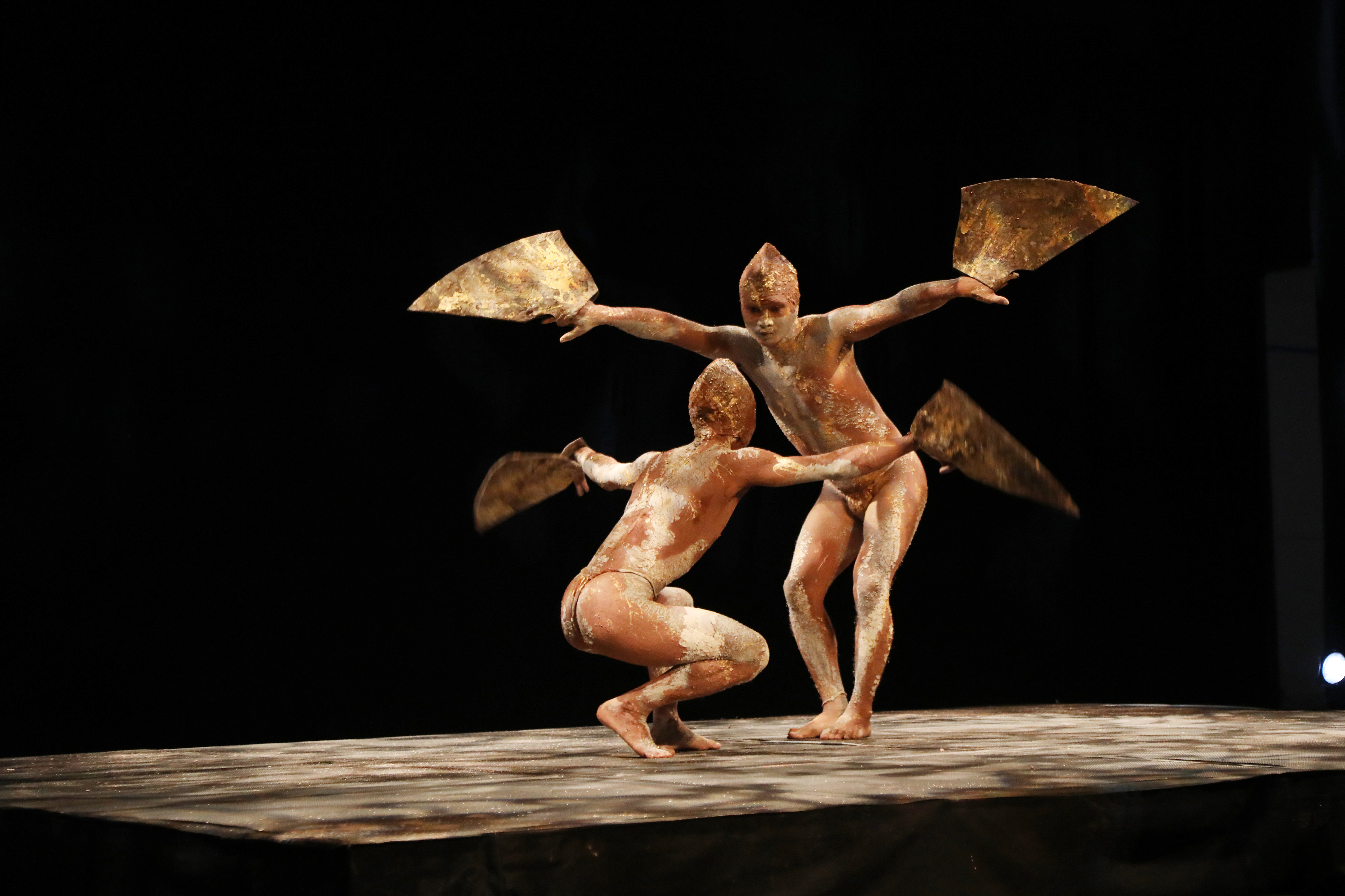 Two creatures face one another, one hovering over the other with arms raised, clutching triangular 'wings.'