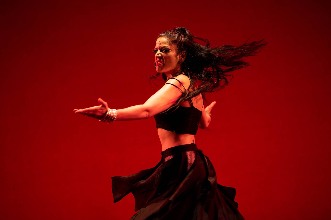 Woman with hire flying, a fierce look on her face, with bare arms extended horizontally. 