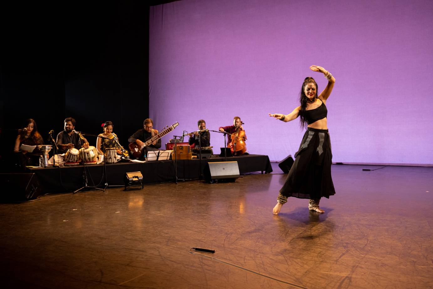 Woman in abbreviated black top and black skirt dancing in front of six musicians.