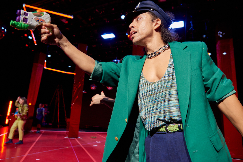 man in a green jacket and police cap,pointing an obviously kiddie  toy gun in the air, and looking anxious