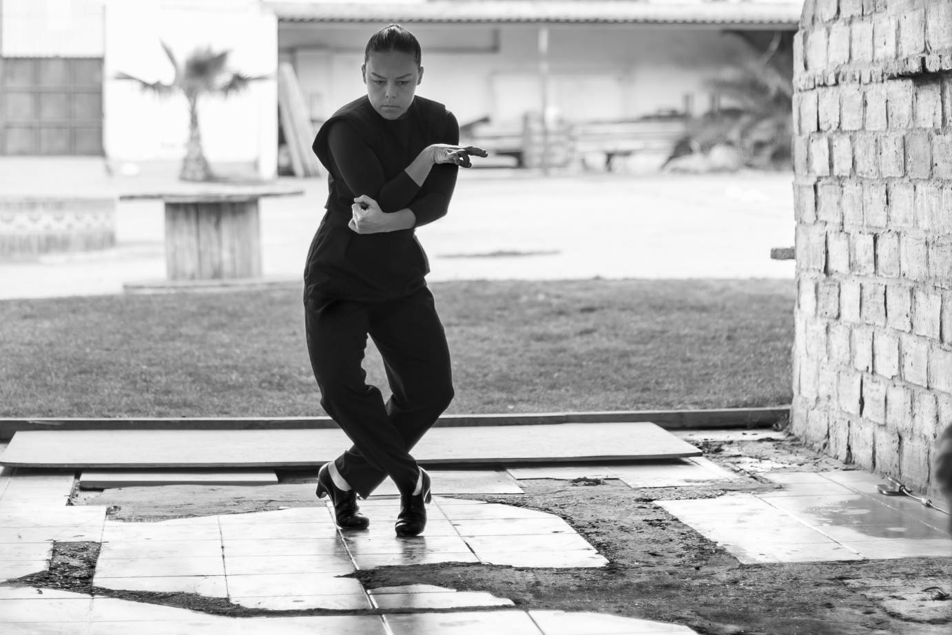 Rocio Molina crosses her arms and legs, bent at the joints, against the backdrop of her farmhouse