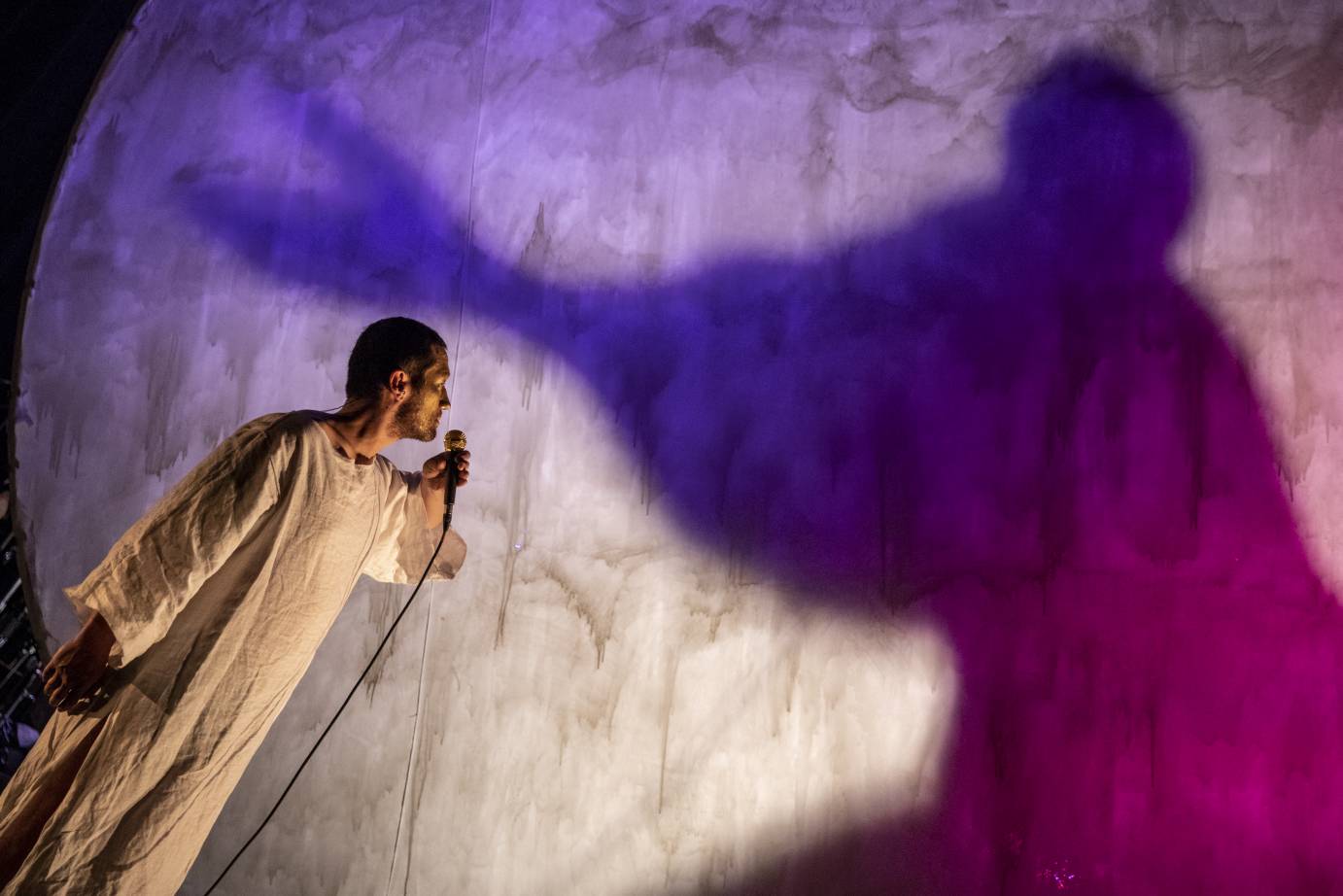 A man stands with a microphone, staring at shadow in a huge paper moon