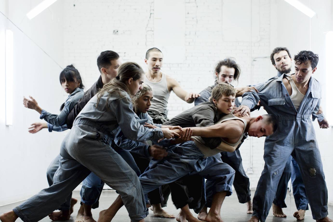 Dancers in coveralls clump together, some touching others