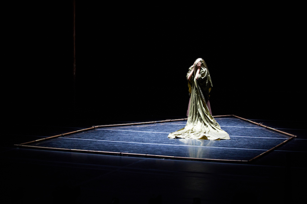 a figure center stage totally covered with a green cloth.they grab their covered face