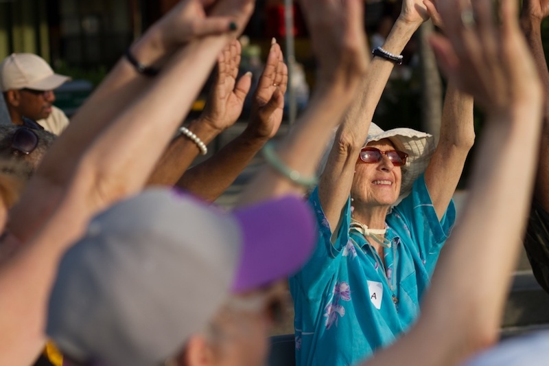 A group of senior dancers huddle together and raise their arms up the sunny sky