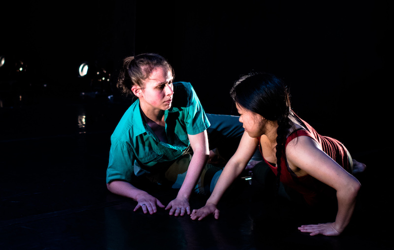 Two dancers lay on the group and stare at one another.