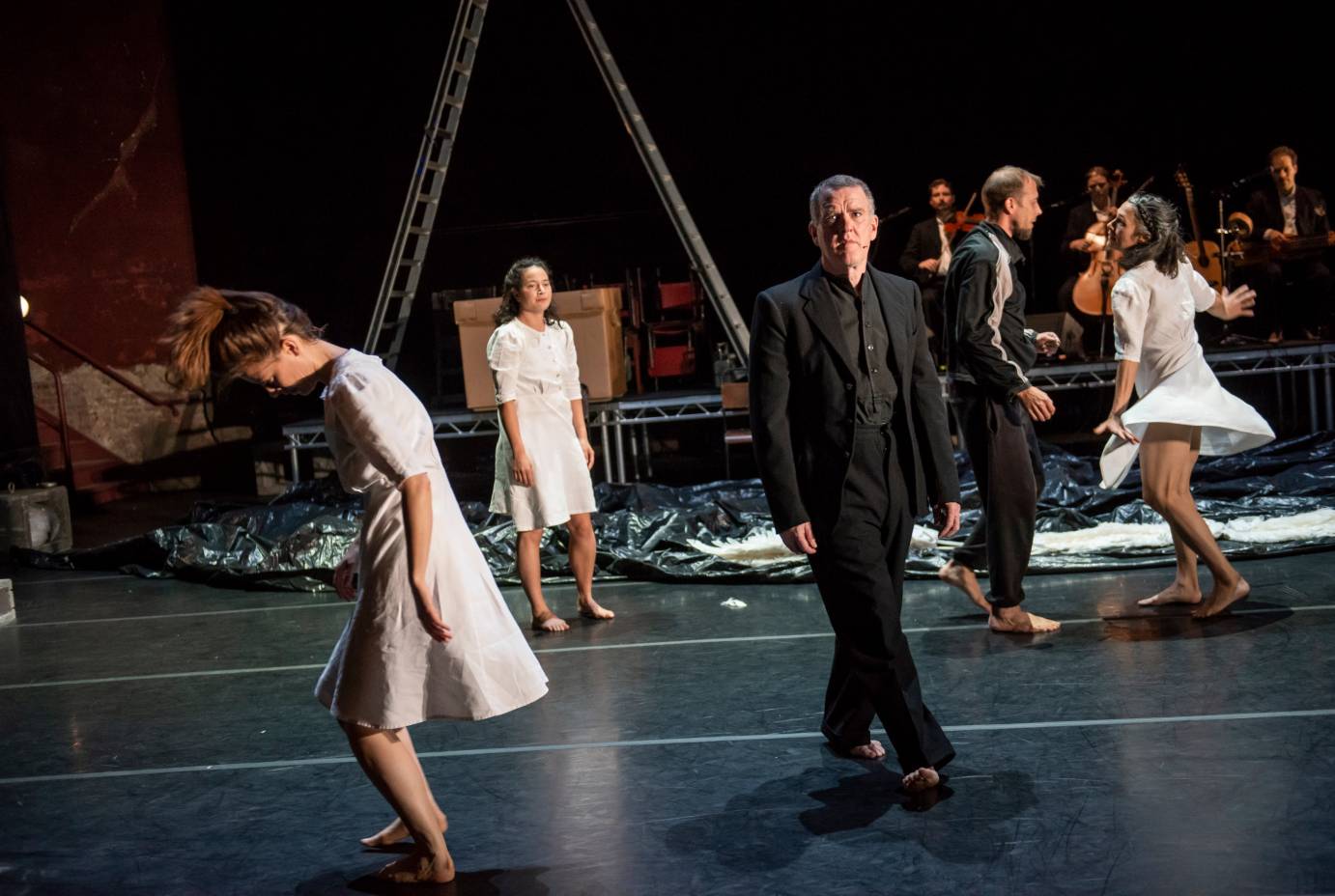 Mikel Murfi stands centerstage as women in white walk around him