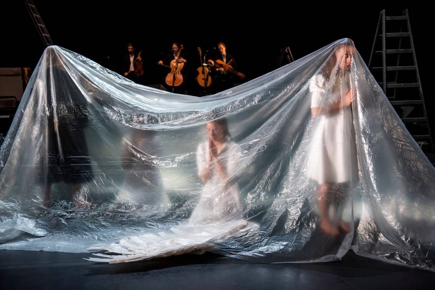 Women make prayer hands while covered by a clear tarp