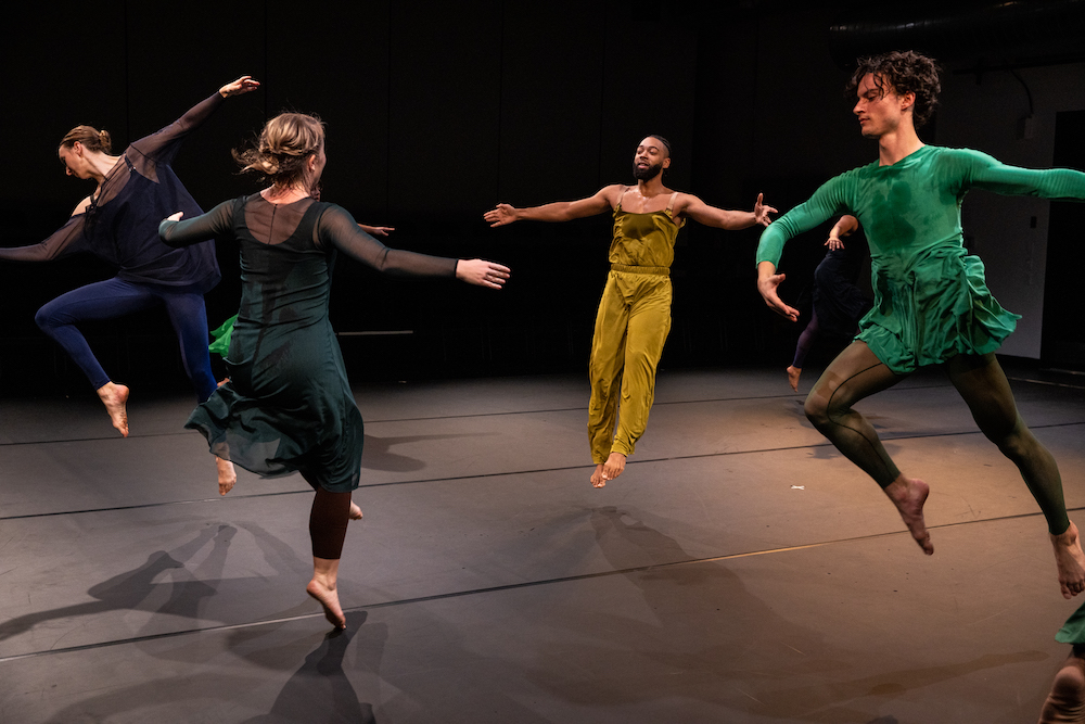 dancers in colorful clothes jump in unison but maintain seperate ways of being in space 