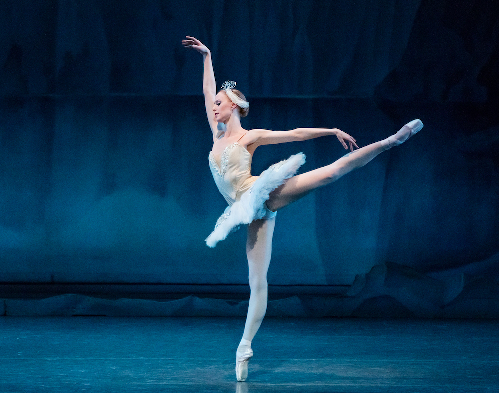 Ballerina in short white tutu in arabesque en pointe, she is performing in Balanchine's Swan Lake