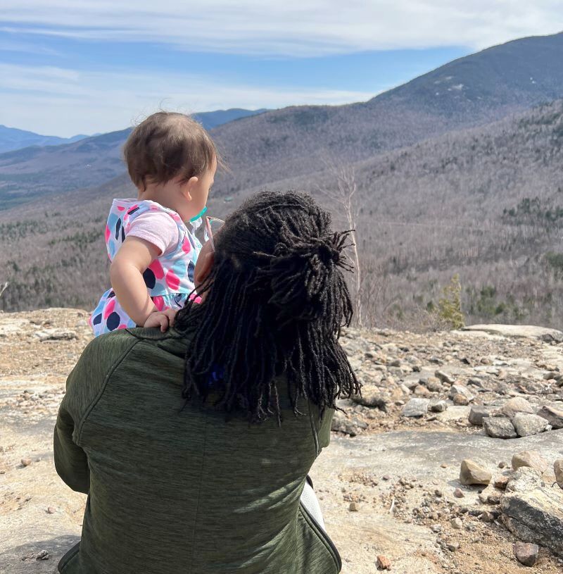 a picture of Tiffany Rea Fisher holding her daughter and staring out at the magnificent landscape of the Adirondacks..